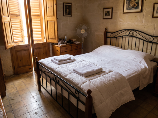 Neatly made bed with fresh white linen and folded towels, Maltese apartment bedroom