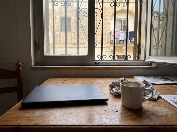 Laptop closed on a kitchen table beside a coffee cup, Maltese apartment