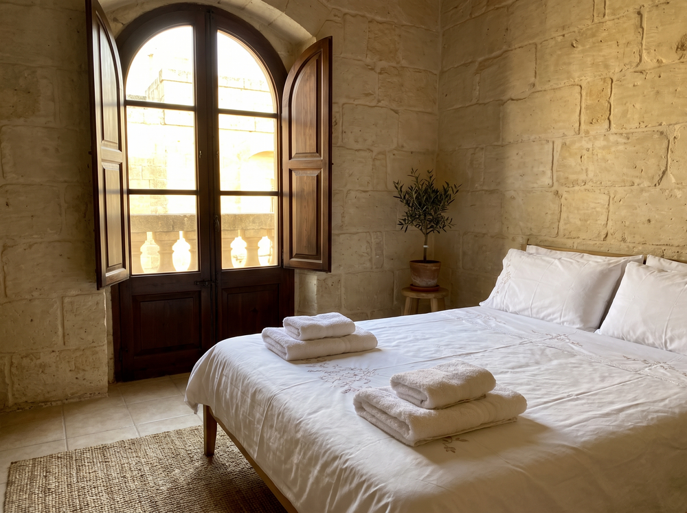 Made bed with folded towels in a bright Maltese apartment bedroom